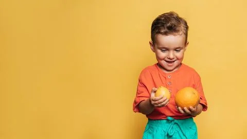 Studio shot of a smiling boy holding a fresh lemon and orange on a yellow Stock Photos