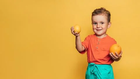 Studio shot of a smiling boy holding a fresh lemon and orange on a yellow Stock Photos