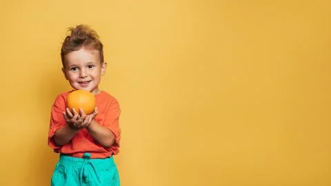 Studio shot of a smiling boy holding a fresh lemon and orange on a yellow Stock Photos