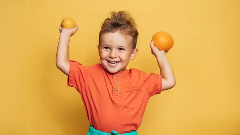 Studio shot of a smiling boy holding a fresh lemon and orange on a yellow Stock Photos