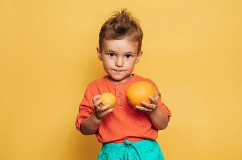 Studio shot of a smiling boy holding a fresh lemon and orange on a yellow Stock Photos