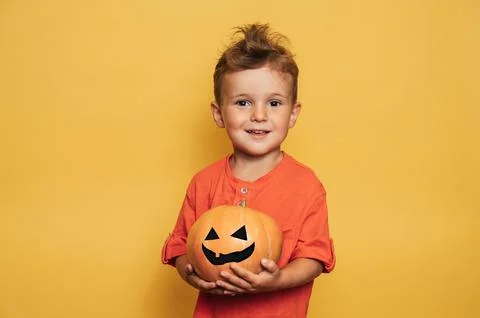Studio shot of a smiling boy holding a Jack O'lantern made of pumpkin on a Stock Photos