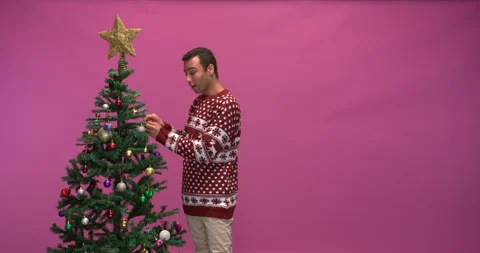 Studio shot of a smiling man decorating a christmas tree, slow motion Vídeos de archivo 140358002