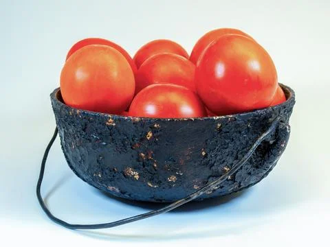 Studio shot of a very battered, burnt and old metalic pot with red tomatoes o Foto stock