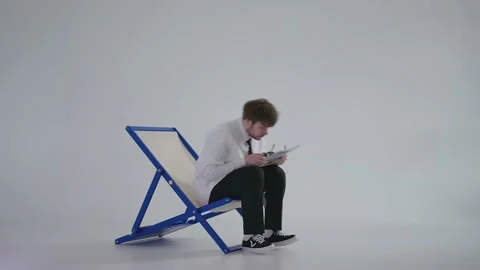In the studio, on a white background, a hipster guy sits on a blue stylish Stock Footage 239449013