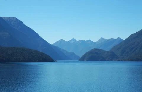 A study in blue - a clear blue sky, blue water and blue mountains. Stock Photos