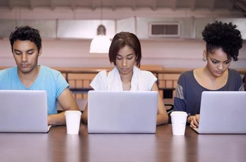 Study group dynamics. Studio shot of three students sitting at a desk working on 库存照片