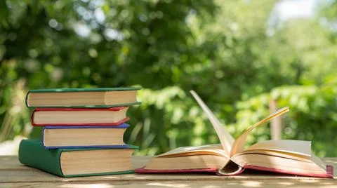 Studying in summer concept. Open book on a wooden table in a garden, sunny su Stock Photos