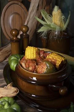Stuffed bell peppers with corn on the cob stewed in tomatoes,still life on wood Stock Photos