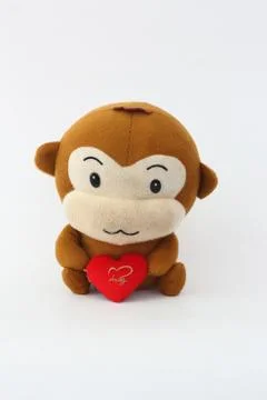 Stuffed brown monkey holding a red heart on a white background. Stock-Fotos