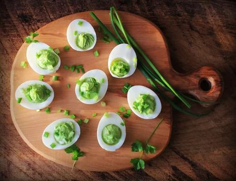 Stuffed deviled eggs appetizer with avocado and leek on cutting board. Top vi Stock Photos