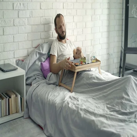 Stuffed man finishing eating breakfast lying on bed at home Stock Footage 69730126