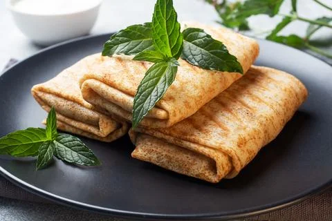 Stuffed thin pancakes rolled into rolls are grilled on a black plate with min 스톡 사진