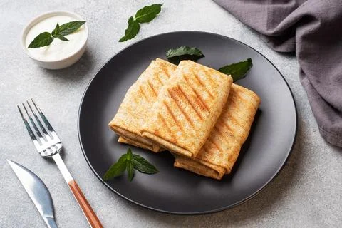Stuffed thin pancakes rolled into rolls are grilled on a black plate with min Stock-Fotos