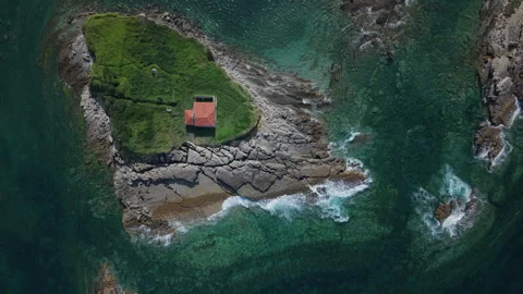 Stunning aerial top-down view of a small red-roofed chapel on a rocky, grassy Видео 336326926