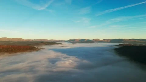 A stunning aerial view of a mountain range shrouded in thick fog and bright sky. Stock Footage 296964368