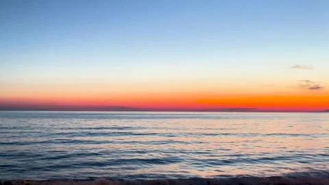 Stunning beach sunset with vibrant orange hues reflecting over the calm ocean Stock Footage 297429874