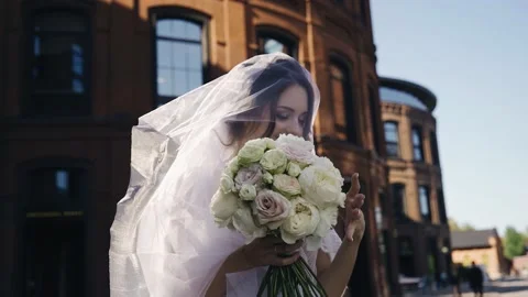 A stunning bride with a veil on her head and a bouquet of flowers in her hands Stock Footage 166059802
