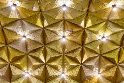 A stunning geometric gold ceiling pattern with bright lights illuminating 스톡 사진