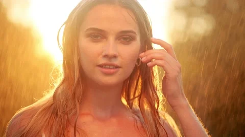 Stunning golden sun rays shine on playful young woman enjoying a summer rain Stock Footage 220578152