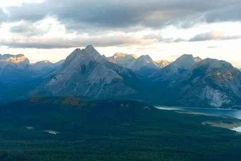 Stunning mountain range under a cloudy sky, green forest in the foreground. Stock Photos