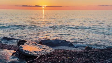 A stunning orange sunset over the sea with soft, gentle waves washing onto .. Stock Footage 345834119