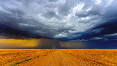Stunning storm clouds gathering over golden wheat fields along dusty rural road Stock Footage 343696674