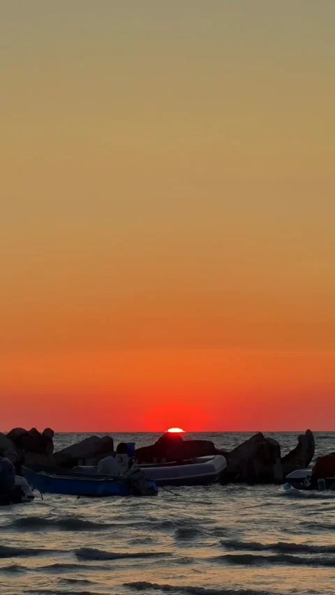 Stunning sunset behind rocks and boats on tranquil ocean horizon Stock Footage 311831129