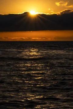 Stunning sunset over the ocean with dramatic sunlight beams and reflective water Photos