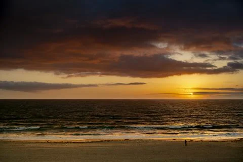 Stunning sunset over the ocean with dramatic clouds and a solitary figure o.. Fotos de archivo