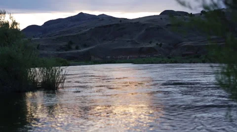 STUNNING SUNSET REFLECTION ON SERENE DESERT RIVER WITH LARGE HILLS IN BACKGROUND Stock Footage 52079354