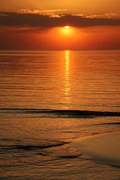 Stunning vertical sunset view over a tranquil sea beach, featuring wet sandbars Stock Photos