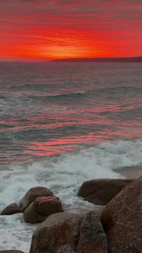 Stunning vibrant sunset over the ocean with crashing waves and rocky shoreline Stockbeeldmateriaal 334163355