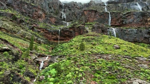 Stunning view of multiple waterfalls streaming down the rocky, green cliffs of Stock Footage 332600830