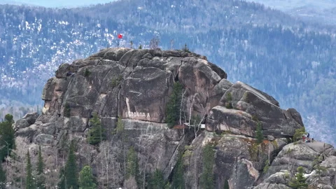 Stunning view of a rocky summit with a flag in the distance surrounded by pine Stock Footage 292009641