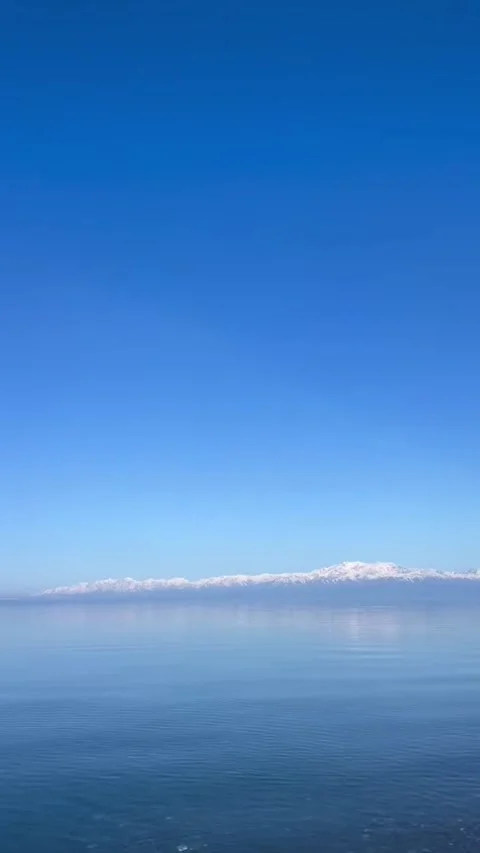 Stunning view of snowcapped mountains across a calm, clear blue lake under a Vidéo 334353467