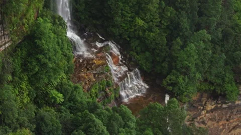 A stunning waterfall cascades down a steep cliff into a lush forest below Stock Footage 308315283