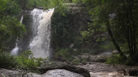 A stunning waterfall cascades over rocks, surrounded by vibrant green foliage. Stock Footage 302263771