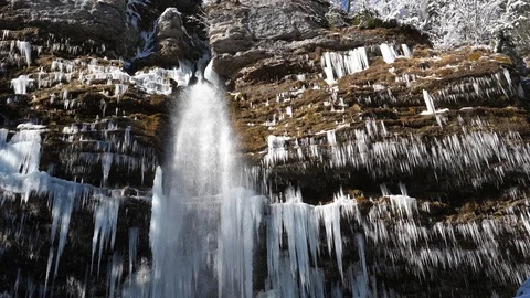 Stunning waterfall falling from the side of a mountain cliff covered in icicles Stock Footage 118972696