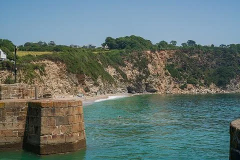 Sturdy Stone Pier Structure Overlooking Turquoise Tidal Water and Steep Gre.. Stock-Fotos