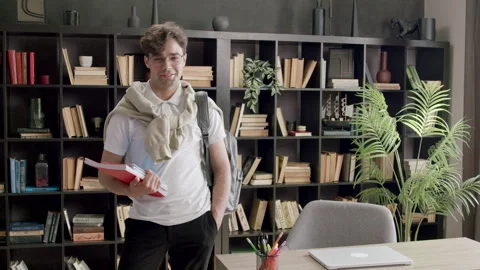 Stylish and handsome student with backpack on his back and books in his hands Stock Footage 316089420