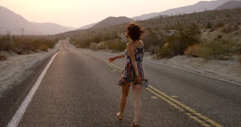 Stylish authentic young woman dances down desert highway just before sunrise Stock Footage
