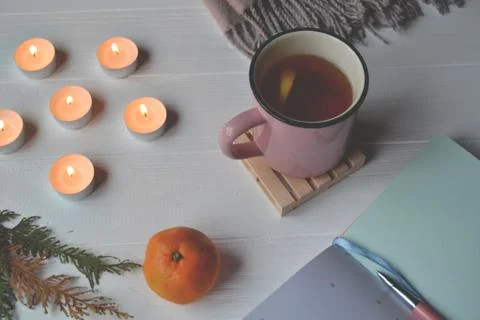 Stylish background with a cup of tea, notebook and lighted candles. Stock Photos