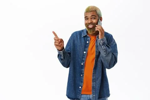 Stylish bearded man points left, talks on mobile phone, calling and showing Фото
