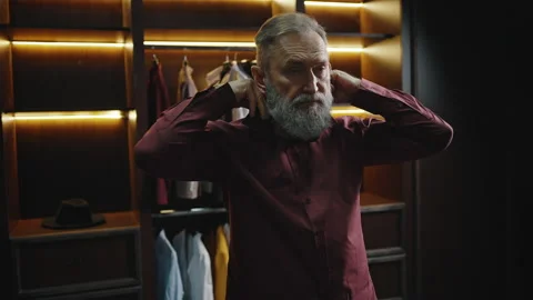 Stylish bearded mature man getting ready in morning, buttoning up his shirt in Stock Footage 196216245