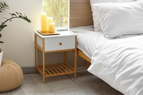 Stylish bedside table with burning candles near cozy bed in bedroom Stock Photos