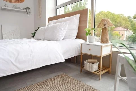 Stylish bedside table with lamp and houseplant near cozy bed in bedroom Stock Photos