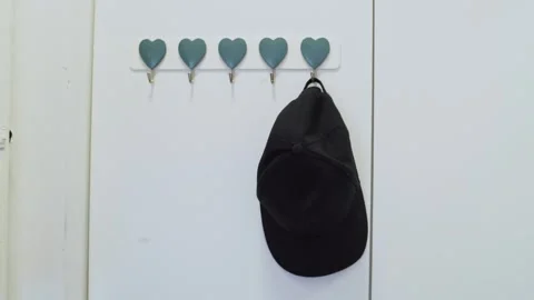 A Stylish Black Hat Elegantly Hanging on HeartShaped Hooks in a Beautiful Stock Footage 282433561