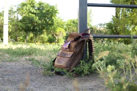 Stylish brown backpack resting against a gate in a lush green park Фото
