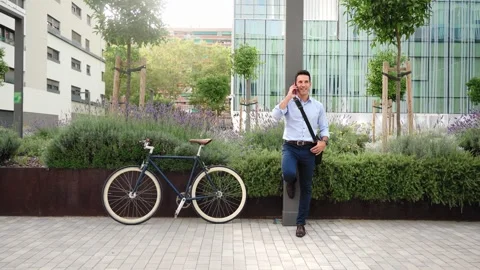 Stylish Businessman with bike using cell phone to call outside the workplace Stock Footage 306659346